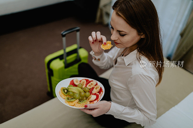 一个女人提着箱子来到酒店房间吃水果