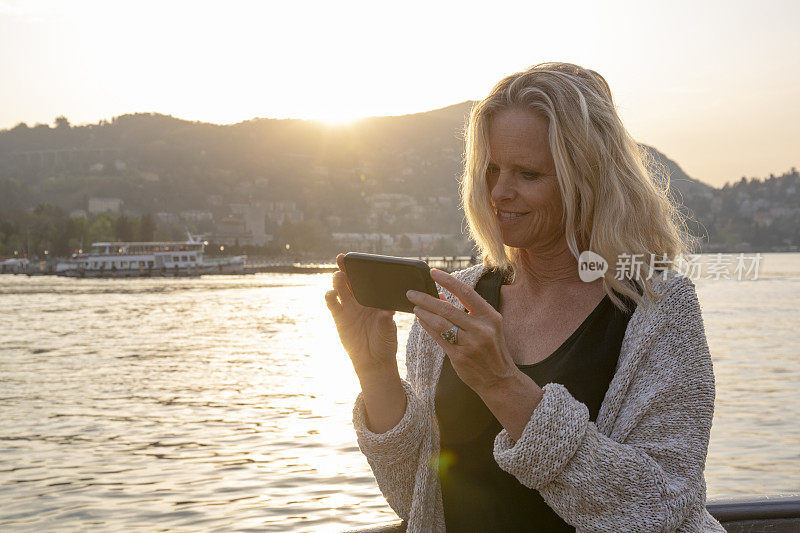 一个成熟的女人用手机拍摄科莫湖的日出