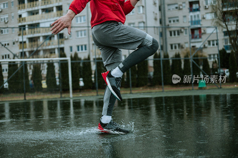 一个男人的腿，谁是跳跃在水坑中训练在雨天