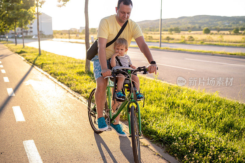 父亲骑着自行车，儿子坐在婴儿座椅上