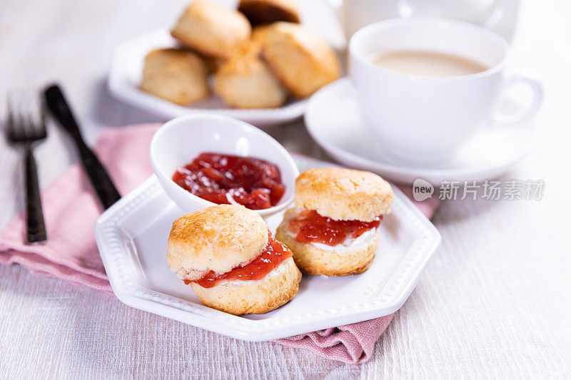 奶油果酱英式烤饼和一杯茶放在白色的桌子上。