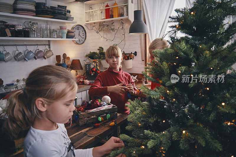 小女孩有乐趣的装饰品和圣诞灯装饰圣诞树