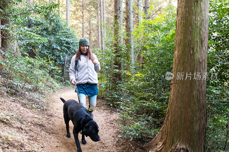 一个女人带着她的狗在山间森林的小路上徒步旅行