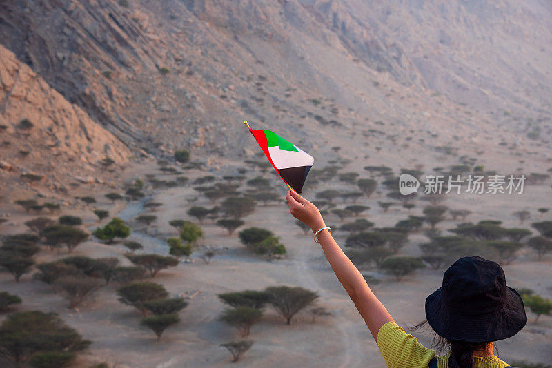 在沙漠山区，一名妇女举着阿联酋国旗