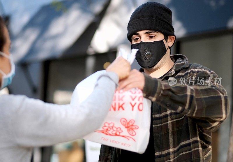 一名失业青年戴着防护口罩，从慈善中心领取免费餐食