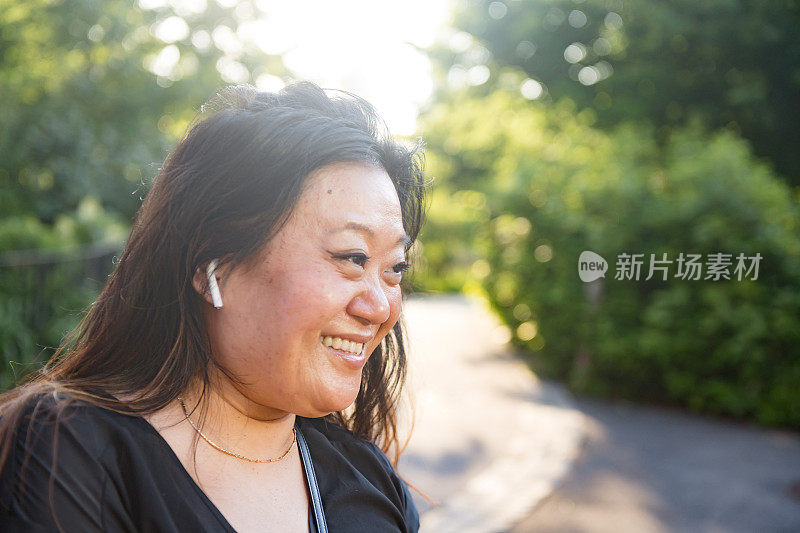 微笑的亚洲女人在30多岁的户外无线耳机在布鲁克林夏天