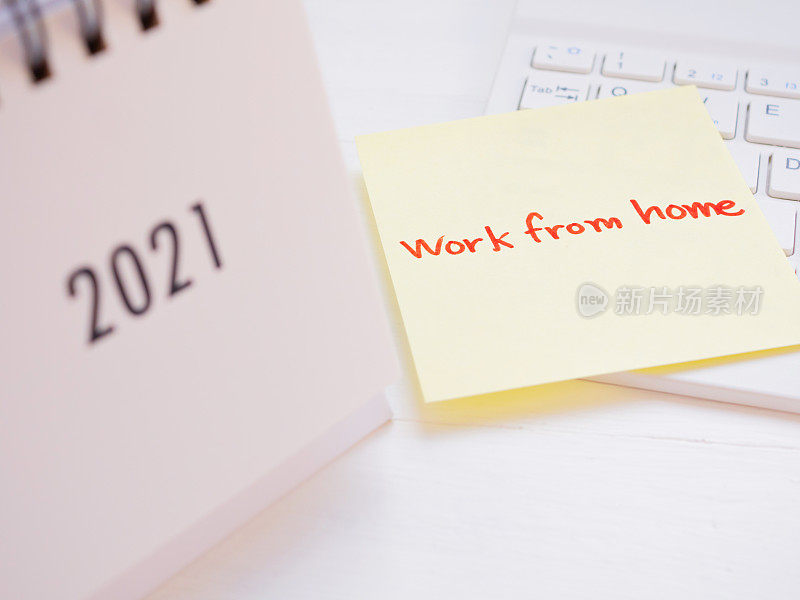 在白色木质背景的键盘上写上“在家工作”的手写信息。2021年的前景是模糊的。