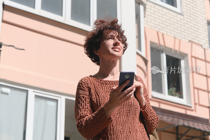 成熟的女人正在寻找城市里的地址。她正在用智能手机上的地图