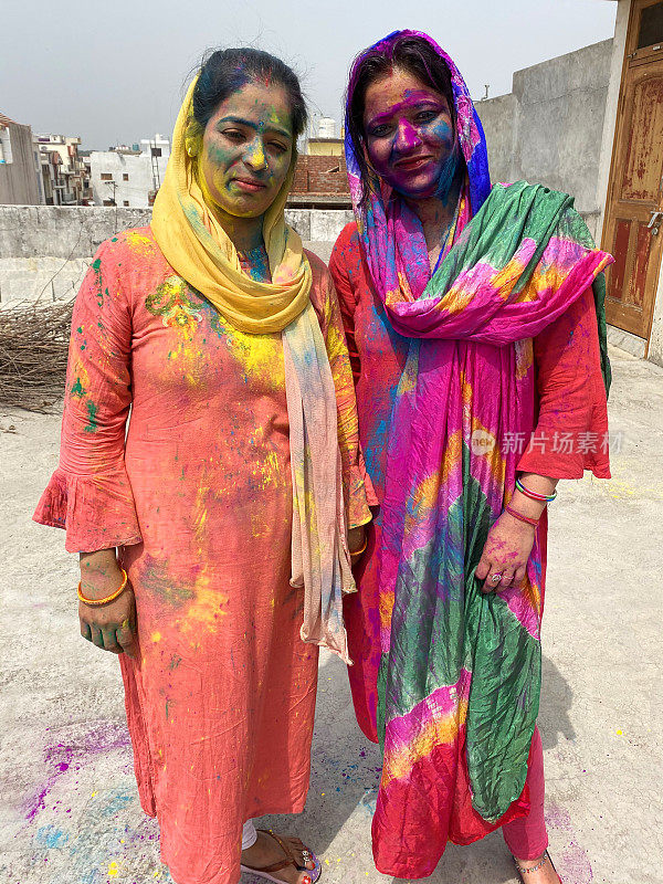印度妇女穿着沙尔瓦·克米兹的传统服装，覆盖着油漆粉的颜色，在胡里节的色彩和爱漆斗争中胡闹，微笑着看着相机