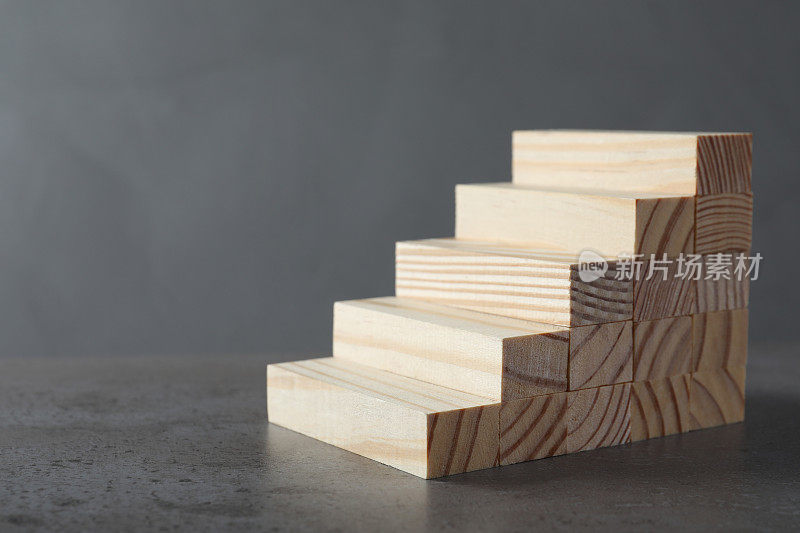 用木块制作的台阶放在桌子上，以灰色为背景，为文字留出空间。职业阶梯
