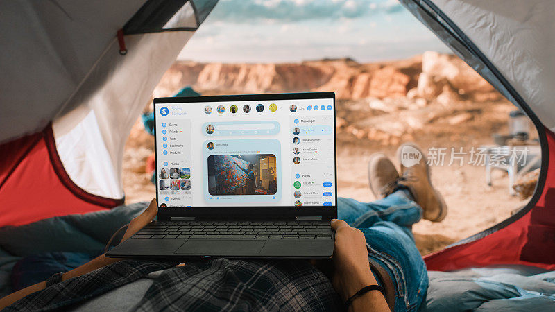 一名游客用笔记本电脑查看社交网络动态和最新照片。在落基山顶的帐篷里休息的旅行者。生活在大自然中的冒险远足者。
