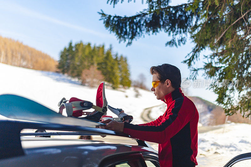 一个英俊的年轻人在树林里把滑雪板从车顶上拿下来