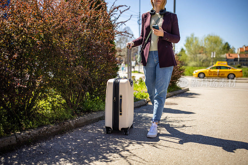 现代年轻女性带着行李箱旅行时使用手机