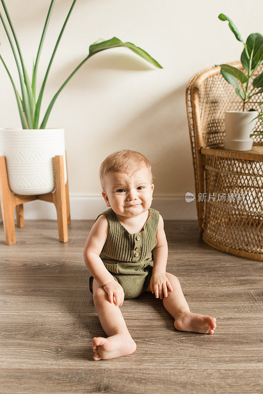 一个脾气暴躁的8个月大的大流行婴儿穿着绿色针织紧身衣在一个海草摩西篮子里玩耍，周围是热带的室内植物