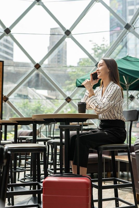 美丽的年轻亚洲女性商务独自女旅行者在机场候机楼的咖啡馆里等待起飞时用智能手机打电话