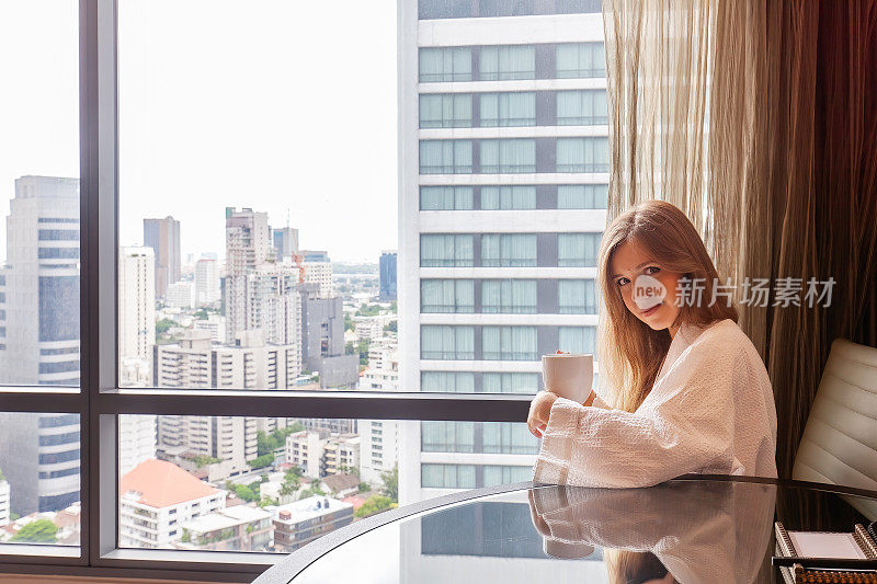 女人穿着浴袍拿着咖啡杯坐在现代酒店或公寓