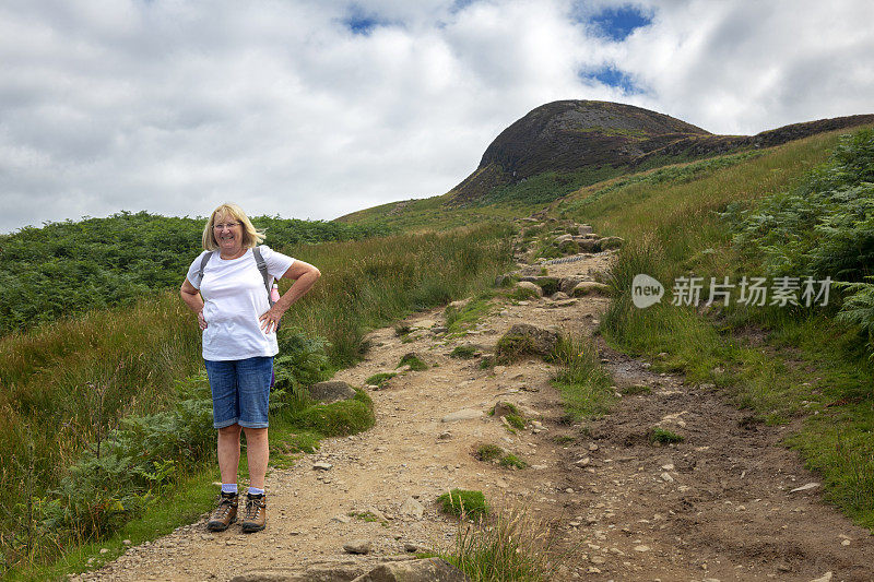 活跃的白人老年女性徒步旅行者从Conic山在巴尔马哈，苏格兰，英国的顶峰走下来