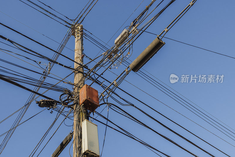 一根木制电线杆上杂乱的互联网和电视电缆、电话线和电线映衬着蓝天。