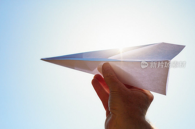 在炎炎烈日下，男人的手正准备将纸飞机发射到晴朗的夏日天空中