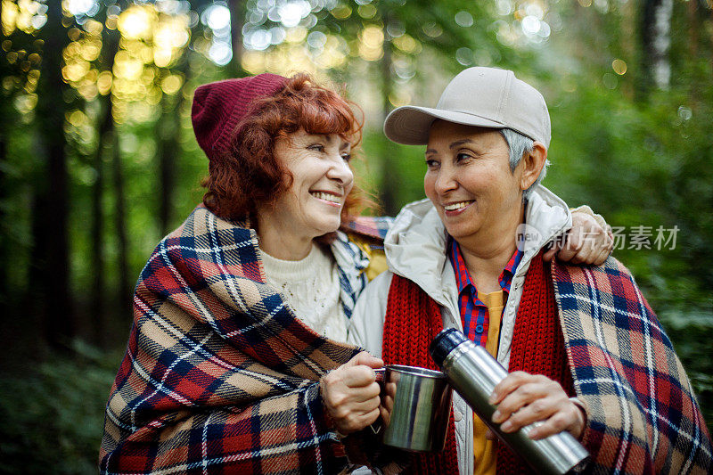 两个老妇朋友走在森林里，从保温杯里倒咖啡，在一起度过了一段美好的时光