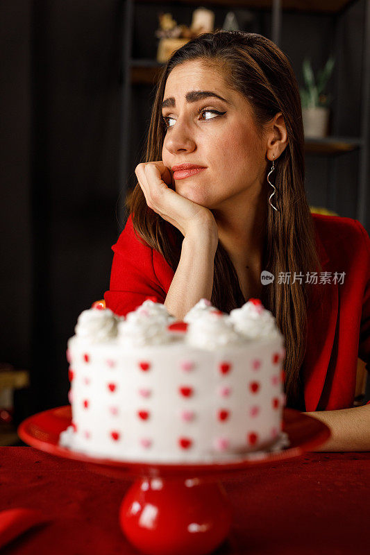 年轻女子坐在桌子前，蛋糕在她面前，做白日梦