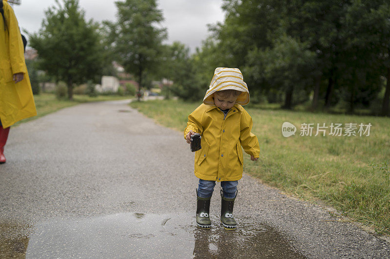 母亲和一个孩子。穿着雨衣的母子在公园里手牵着手