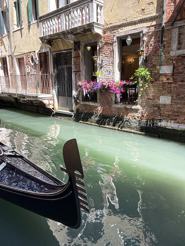 意大利威尼斯，威尼斯泻湖滨水区，船浮在运河水面上的船首金属细节特写，建筑，重点在前景