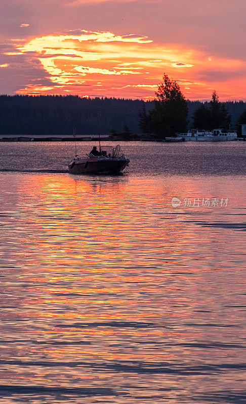 芬兰塞马湖上明亮的夕阳和一艘在夕阳下的机动渔船。夏天的风景