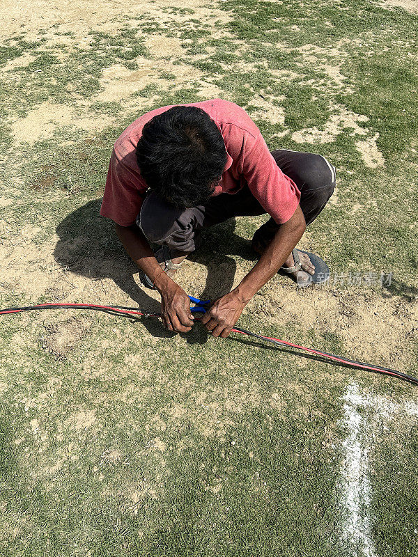印度杂工蹲在烧焦的草坪上连接电缆，炎热的晴天，高架景观