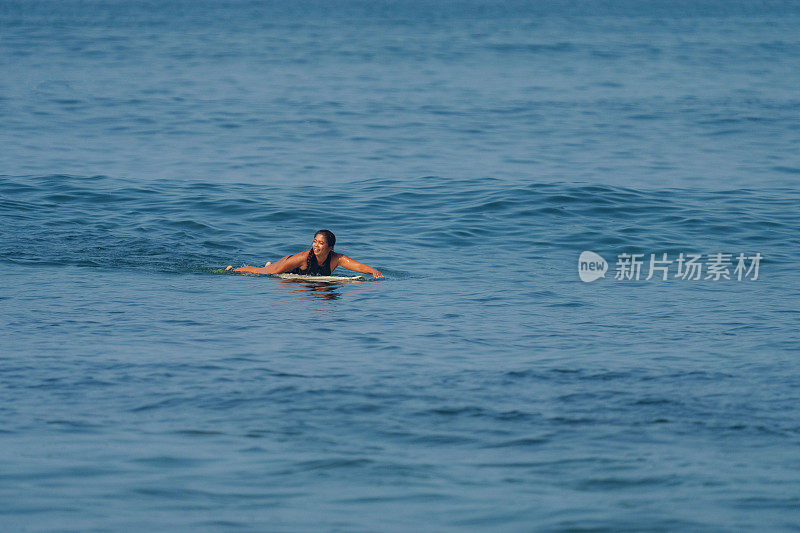 印度尼西亚女冲浪者在海洋中的冲浪板上游泳