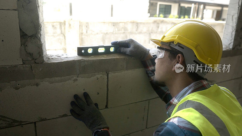 建筑师亚洲使用水位测量仪安装窗户施工现场。在建筑工地使用水平仪的亚洲工人。