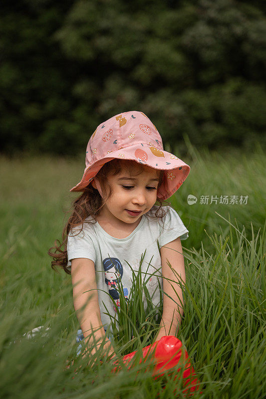 快乐童年的概念，探索你身边的世界。可爱的女孩白天在公园的草地上玩耍。
