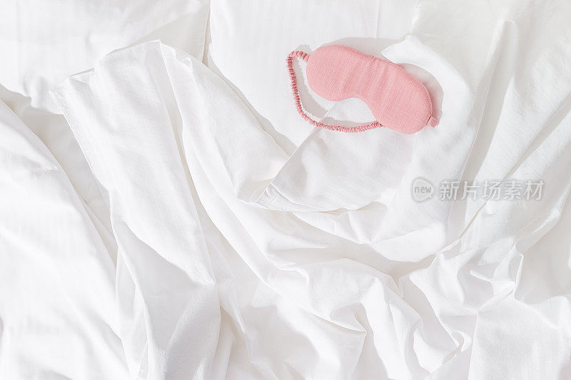 粉红色的眼罩睡觉在白色的床上，极简的生活方式审美平躺照片。女性睡眠面膜，适合最佳睡眠者，适合旅行，舒适放松。好好休息的概念。