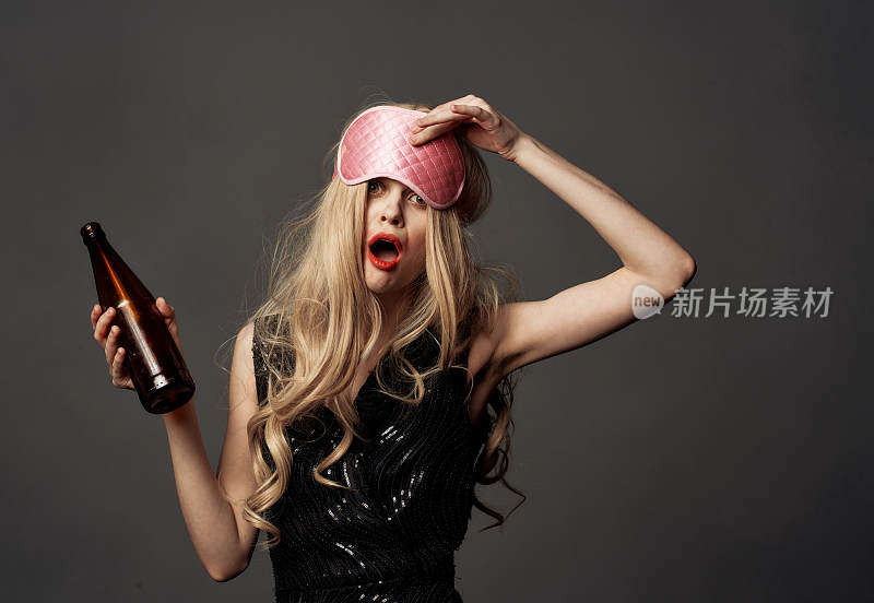 一个喝醉的女人，手里拿着一瓶酒，灰色的背景上，戴着睡觉用的面具