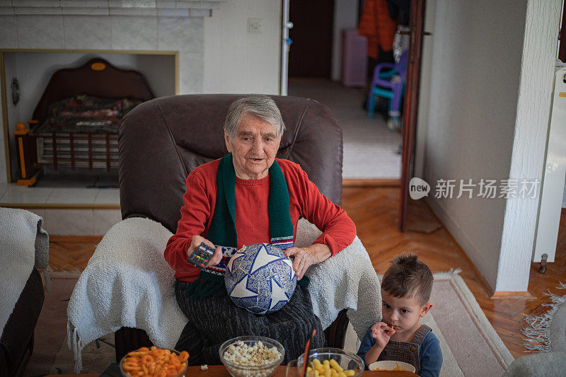 一位祖母正在家里和她的孙子一起看电视上的足球比赛