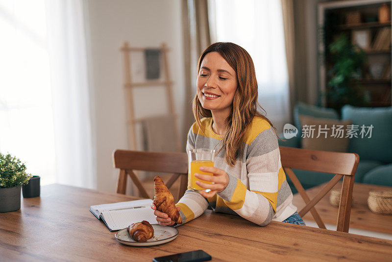 一位年轻女子在家，坐在餐厅的椅子上写笔记