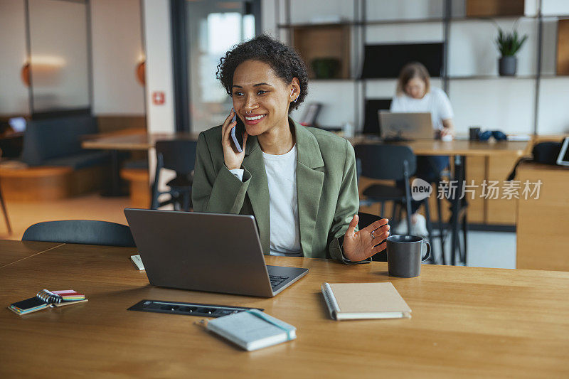 在漂亮的现代联合办公办公室的硬木地板上，桌子上有笔记本电脑和手机的女人