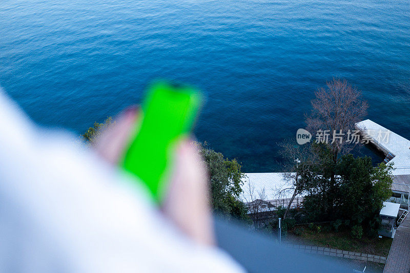 小女孩在海边阳台上用绿屏手机拍照
