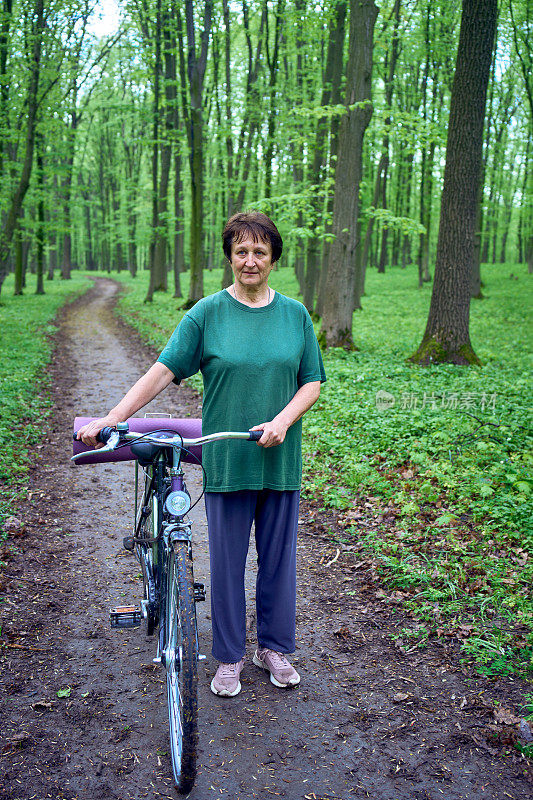 一位老妇人带着自行车和瑜伽垫走在春林里