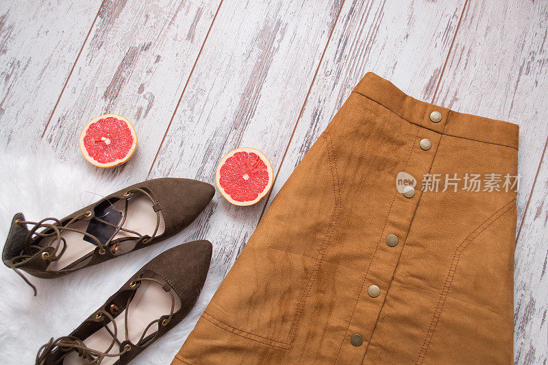 棕色麂皮裙，棕色麂皮鞋，切成两半的葡萄柚。木制背景。时尚的概念。俯视图