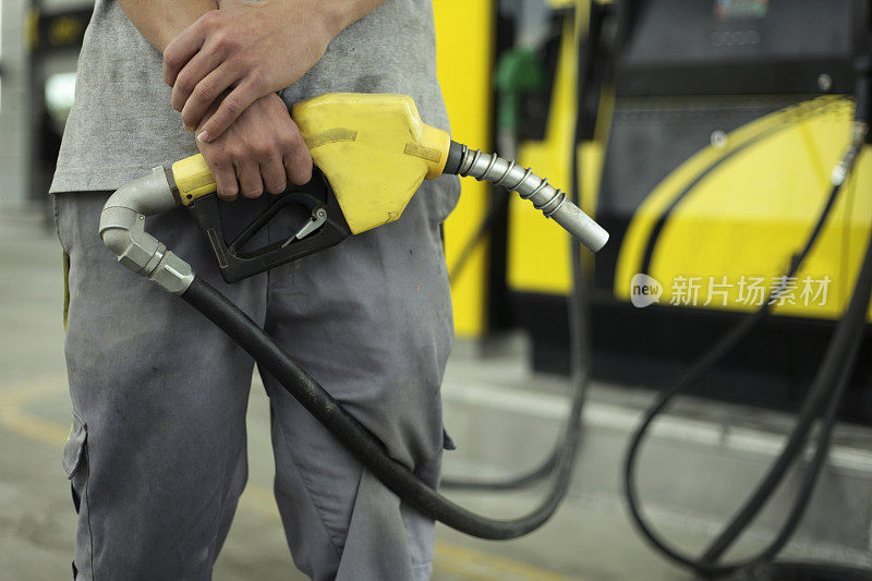 一个穿灰色衣服的人站在加油站拿着黄色的油泵