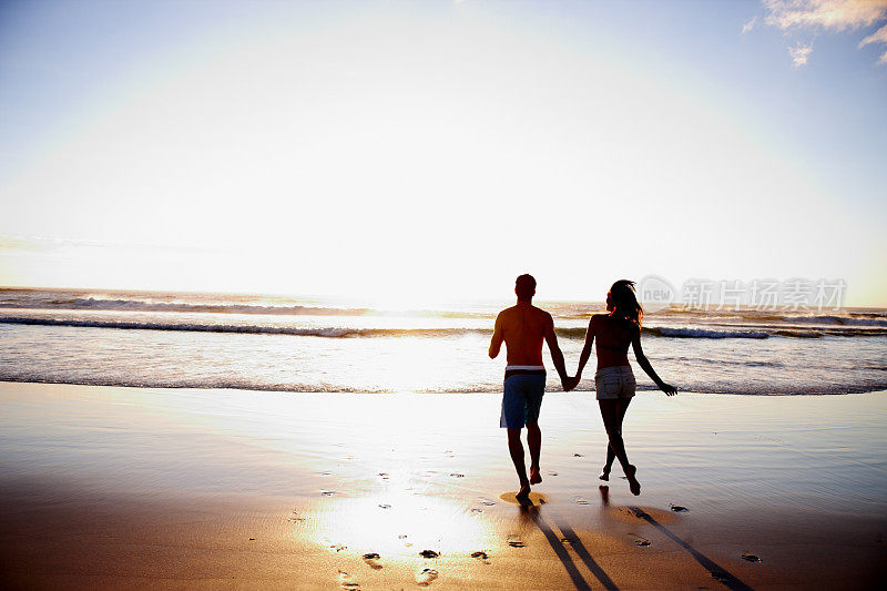 一对在海滩上牵着手的夫妇的后视图