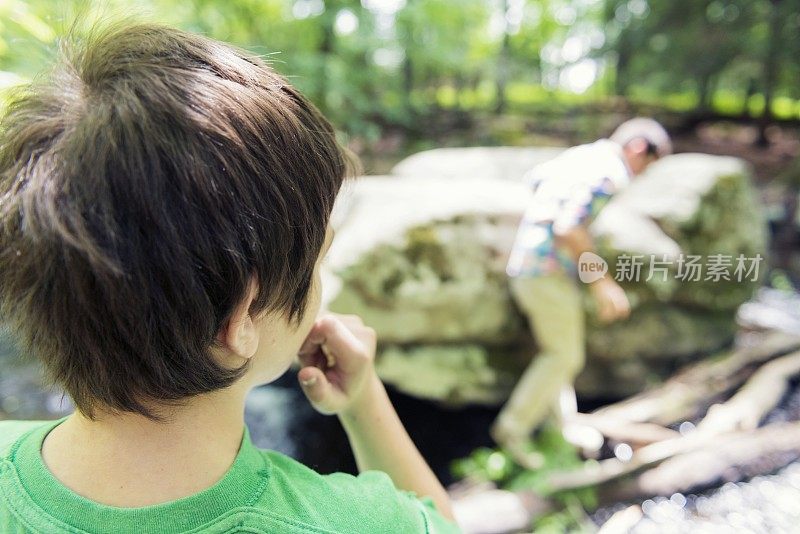 男孩紧张地看着父亲在户外渡过小溪