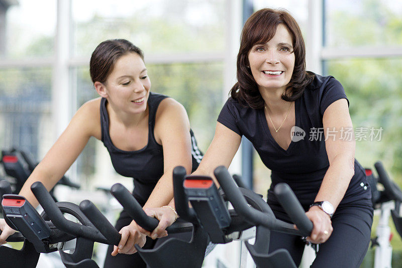 两个成熟的女人在健身房骑自行车