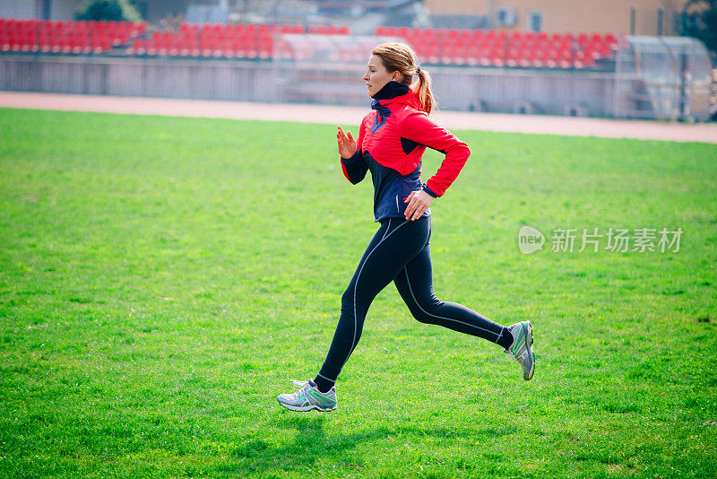 年轻女子在足球场上慢跑，过着健康的生活