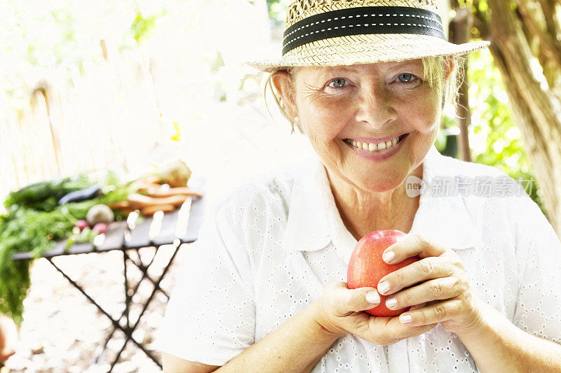 健康的老年妇女在花园里拿着苹果