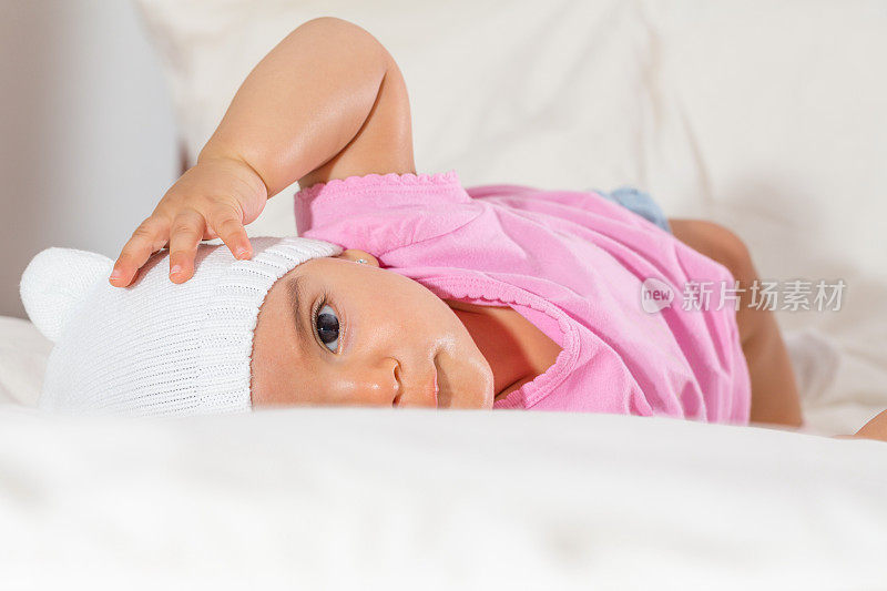 美丽的女婴躺在床上看着相机在她上面