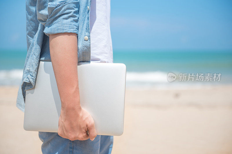 一个男人在海滩上拿着笔记本电脑