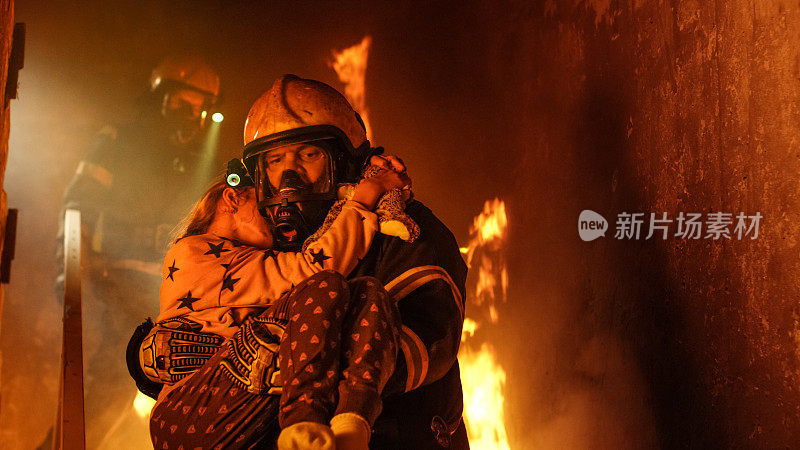 勇敢的消防队员走下燃烧的建筑物的楼梯，将获救的女孩抱在怀里。开火，背景中有一名消防员。