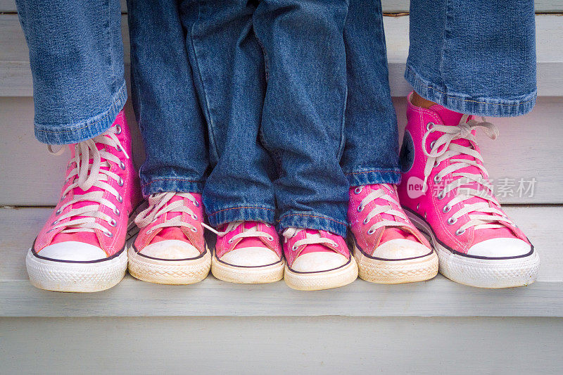 一位母亲和她的两个女儿炫耀她们的粉色运动鞋。